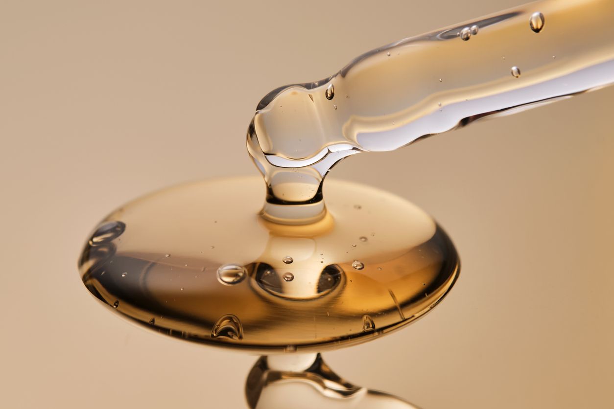 Serum dropper dripping clear formula on a smooth surface, macro view.