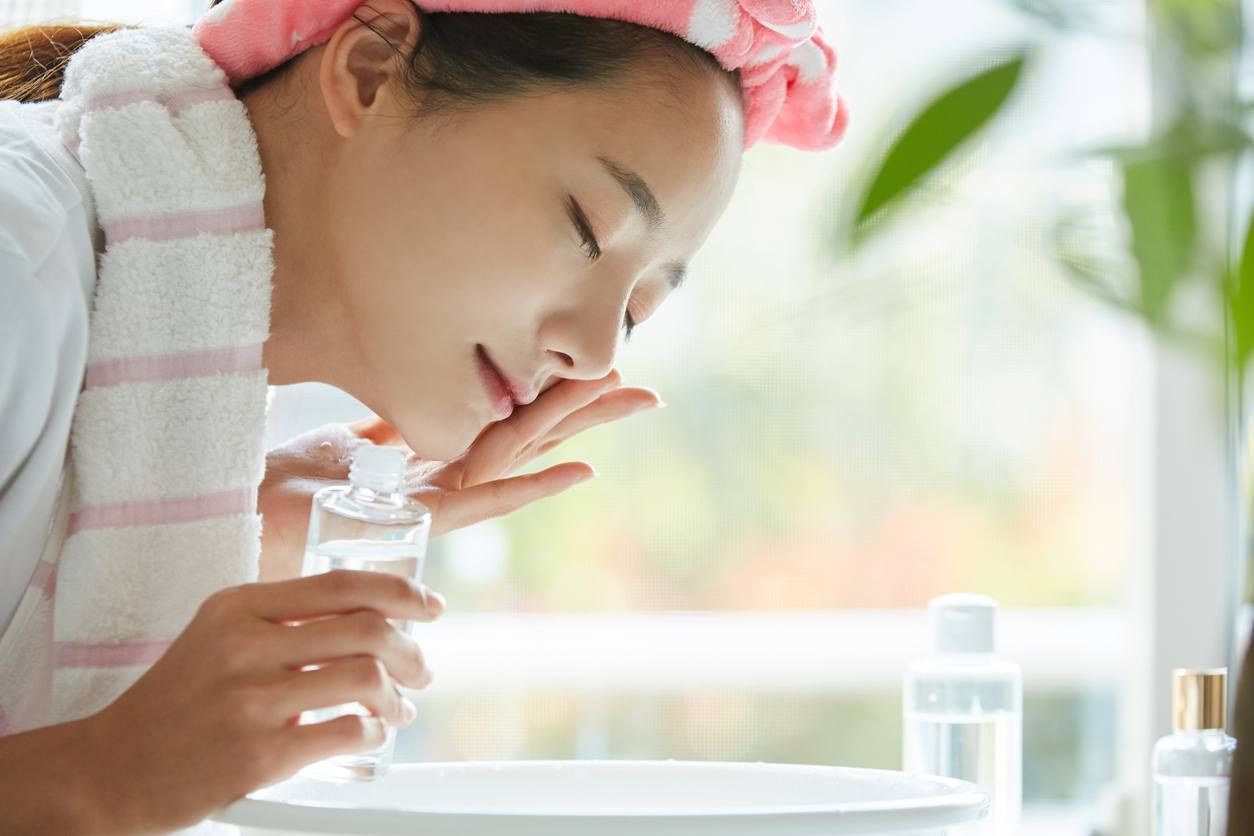 A young woman applying her Korean Skincare Routine at her bathroom sink