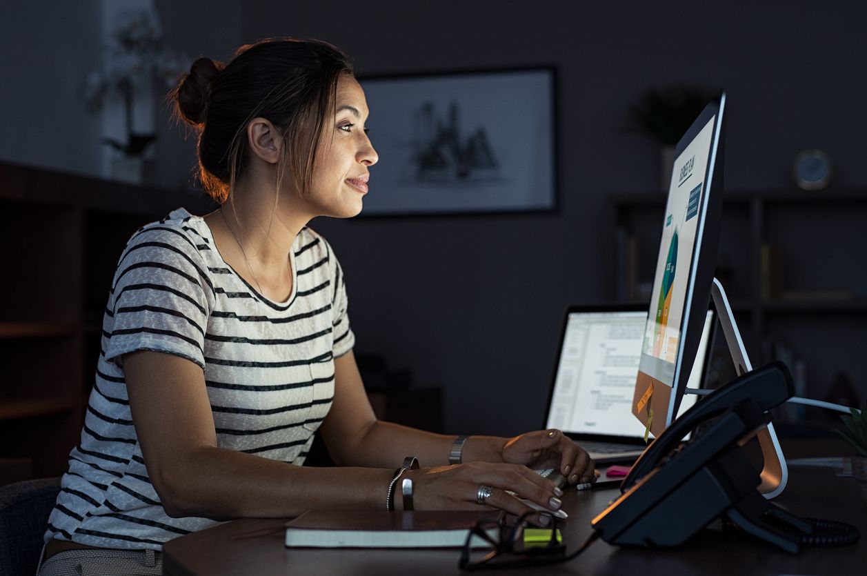 A woman uses her computer at night, exposing her to blue light skin damage