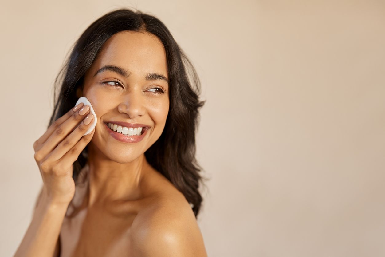 A young woman completes her skincare routine by cleaning her face with a cotton pad