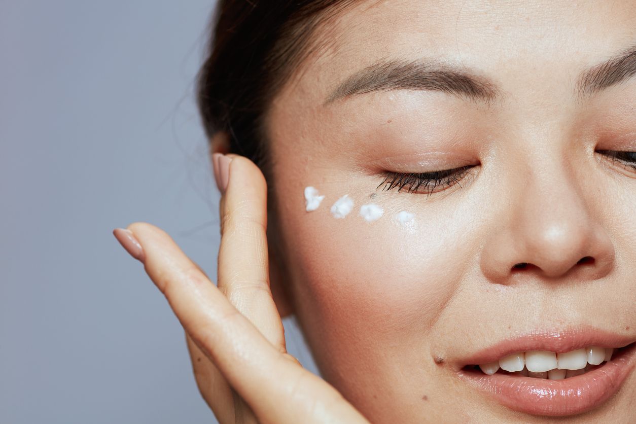 Woman gently applying K-beauty eye cream under eyes to brighten and reduce dark circles.